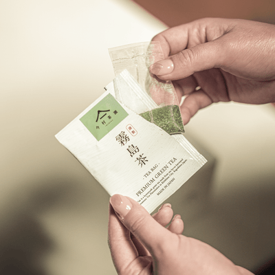 霧島茶ティーバッグの個包装を開けて三角ティーバッグを取り出す手元 / Hands opening an individually wrapped Kirishima green tea bag - 今村茶園